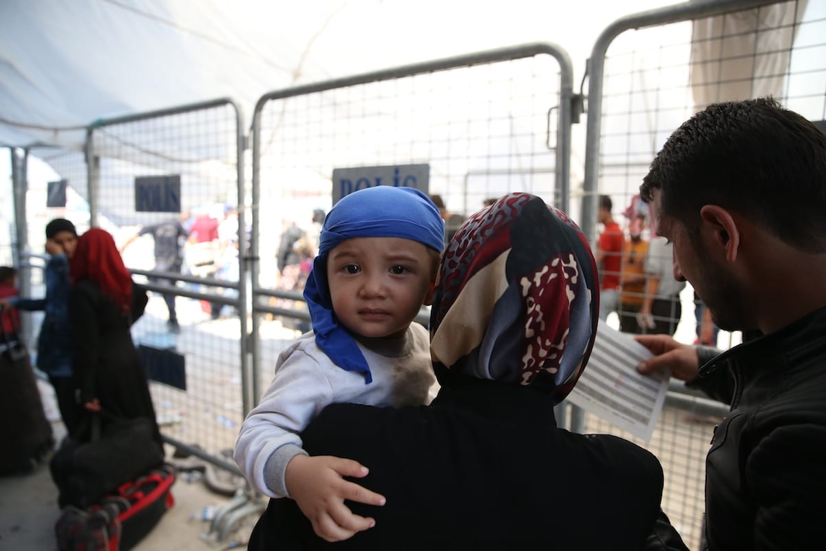 A baby is seen in his mother arms as Syrian refugees pass through Oncupinar border gate to reach their hometowns before Eid al-Adha in Kilis, Turkey on 29 August, 2017 [Ensar Özdemir/Anadolu Agency]