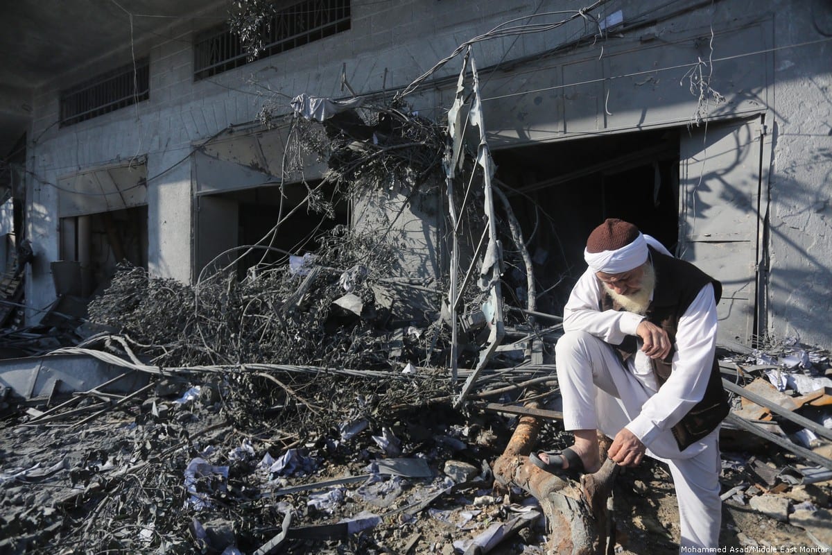 An elderly Palestinian man leans on a tree destroyed and tangled with debris outside a building. 13 November 2018 [Mohammed Asad/Middle East Monitor]