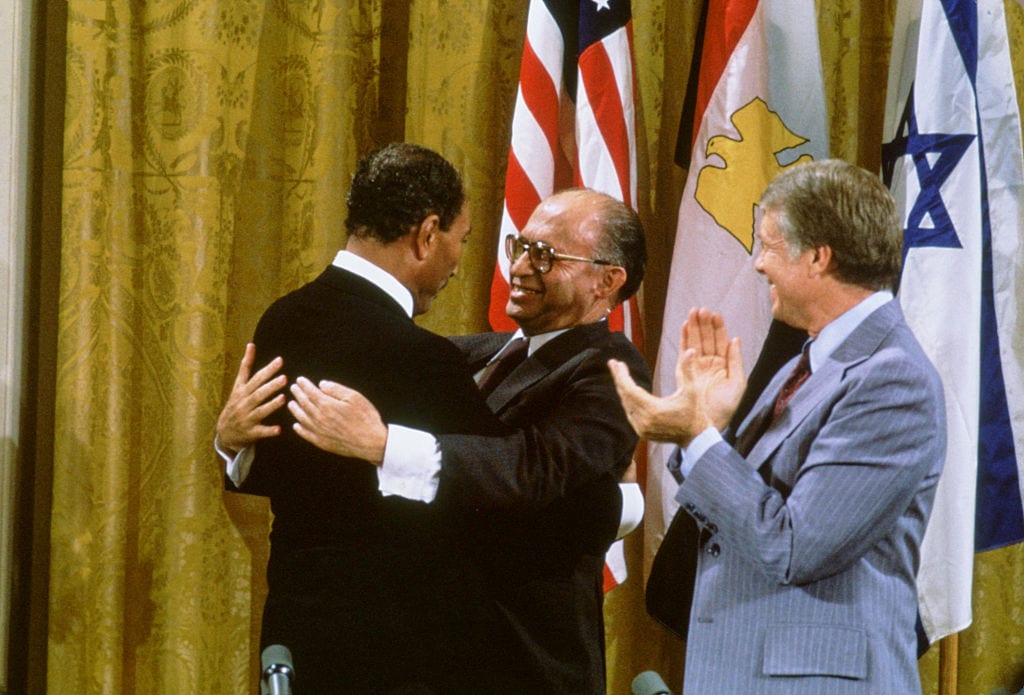 Egyptian President Anwar al-Sadat and Israeli Premier Menachem Begin embrace, while US President Jimmy Carter applauds after signing the Camp David Accords in the East Room of the White House, September 18, 1978, in Washington, DC. [David Hume Kennerly/Getty Images]
