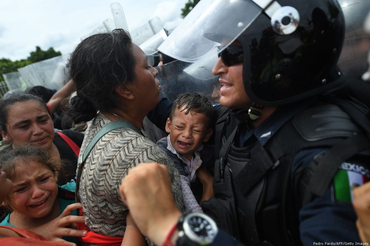 Honduran migrants heading in a caravan to the US, holding up a crying baby while they struggle to cross one of the gates of the Guatemala-Mexico international border bridge in Ciudad Hidalgo, Chiapas state, Mexico, on 19 October, 2018 [PEDRO PARDO/AFP/Getty Images]