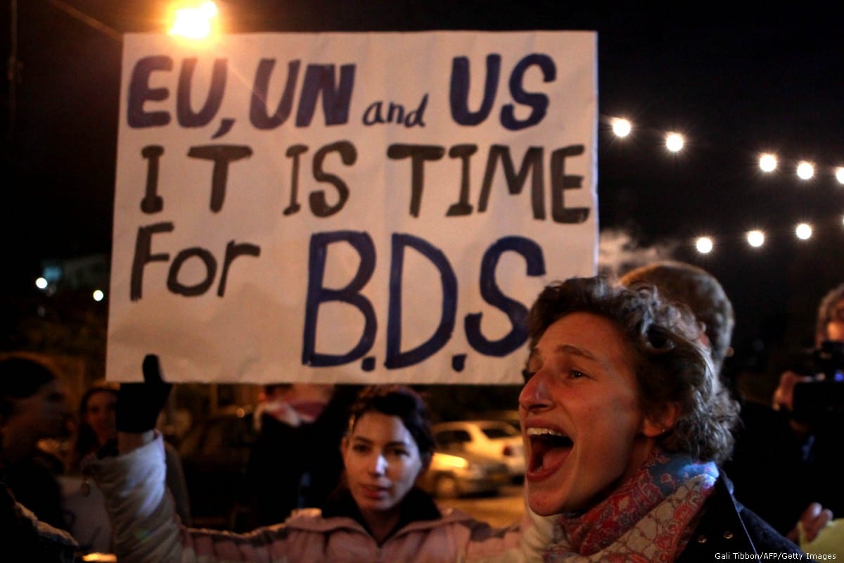 Demonstrators hold a placard urging the international community to support the Boycott, Divestment, and Sanctions (BDS) campaign [Gali Tibbon/AFP/Getty Images