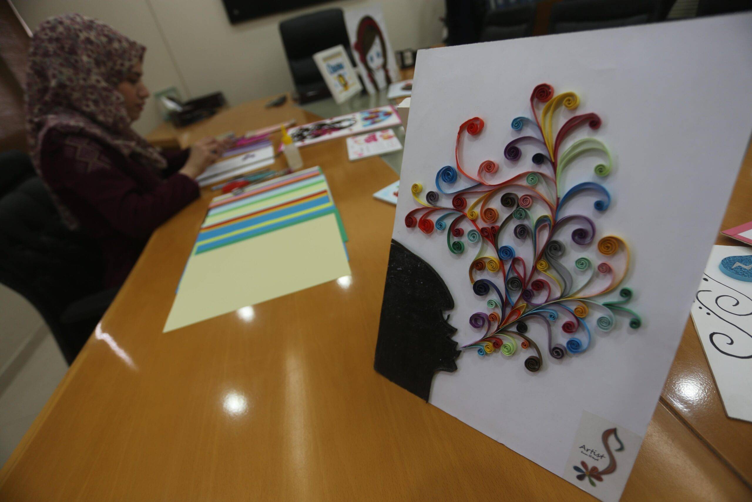 Gaza artist, Iman Al-Tayeb, cuts coloured paper into narrow strips and then curls and glues them to a board to make a 3D piece of art [Mohammed Asad/Middle East Monitor]