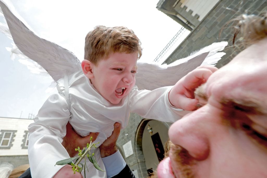 A toddler in angel costume pinches a man as Catholic believers gather outside Greek-Melkite Patriarchal Cathedral of the Dormition of Our Lady to mark Palm Sunday in the capital Damascus in Bab Sharki, Old Damascus on 14 April, 2019 [LOUAI BESHARA/AFP/Getty Images]
