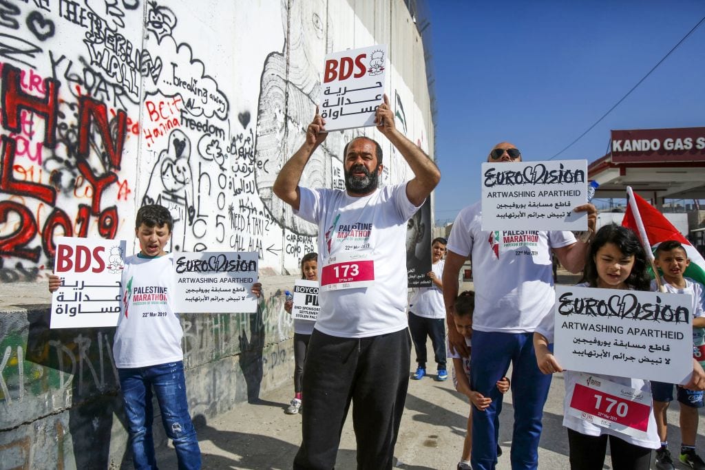 Activists hold placards calling for the boycott of Eurovision along Israel's controversial separation barrier, which divides the West Bank from Jerusalem, during the 7th International Palestine Marathon in the biblical town of Bethlehem in the occupied West Bank on 22 March 2019. [MUSA AL SHAER/AFP/Getty Images]