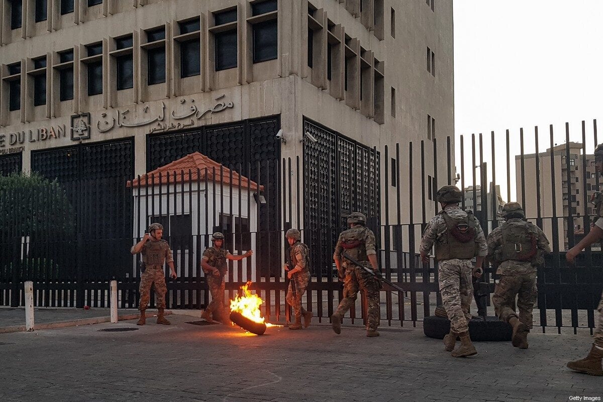 Lebanese Army soldiers roll away a flaming tire from the fence surrounding the local branch of the Banque du Liban (Lebanese Central Bank) as protesters gather to demonstrate against dire economic conditions in the northern city of Tripoli on 11 June 2020. [FATHI AL-MASRI/AFP via Getty Images]