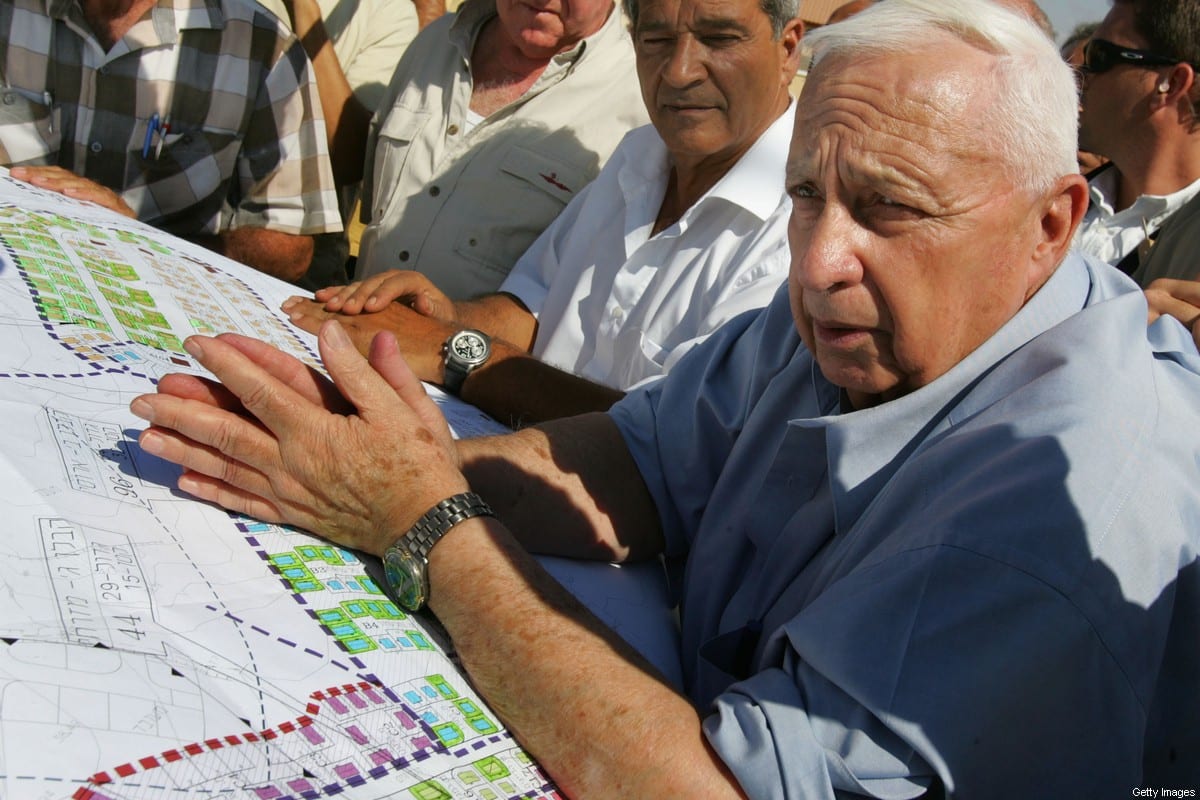 Then Israeli Prime Minister Ariel Sharon leans over housing plans as he meets with contractors who are building temporary housing for settlers due to be evacuated from the Gaza Strip under his disengagement plan July 5, 2005 at the Nitzanim construction site in southern Israel [David Silverman/Getty Images]
