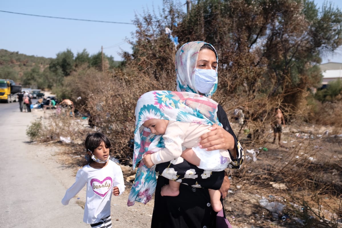 A woman walks with a little girl while carrying a baby on a roadside as many refugees and migrants remain homeless after a fire destroyed the Moria refugee camp on the Greek island of Lesbos, on 16 September 2020. [Aggelos Barai - Anadolu Agency]