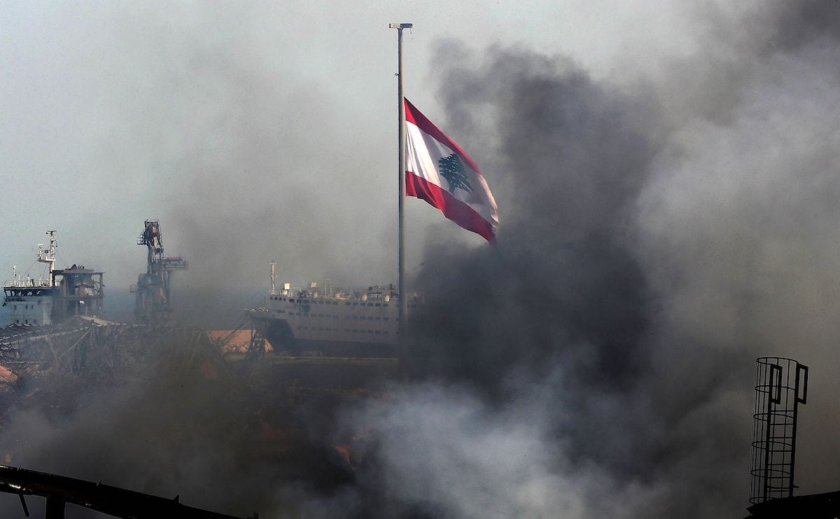 A Lebanese flag flutters amid billowing smoke as firefighters extinguish the remaining flames at the seaport of Beirut, on 11 September 2020 [ANWAR AMRO/AFP/Getty Images]