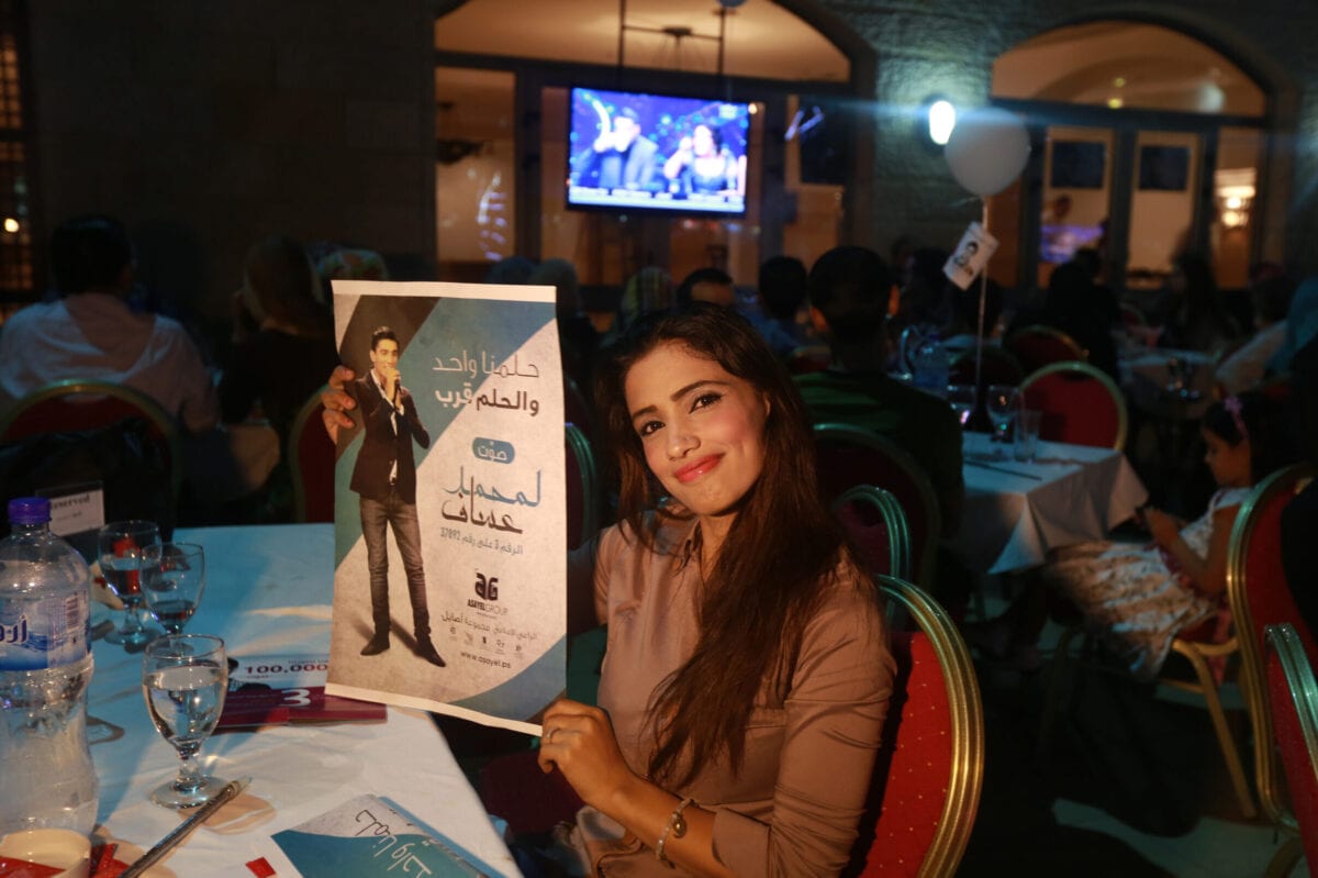 A Palestinian supporter of Mohammed Assaf, a Palestinian finalist on the Arab Idol talent show, holds his poster in Gaza City as she watches his televised performance late on June 21, 2013. Since March, the 22-year-old Gazan's powerful voice has propelled him to the final of a Beirut-based competition that started out with 27. AFP PHOTO/MOHAMMED ABED (Photo credit should read MOHAMMED ABED/AFP via Getty Images)