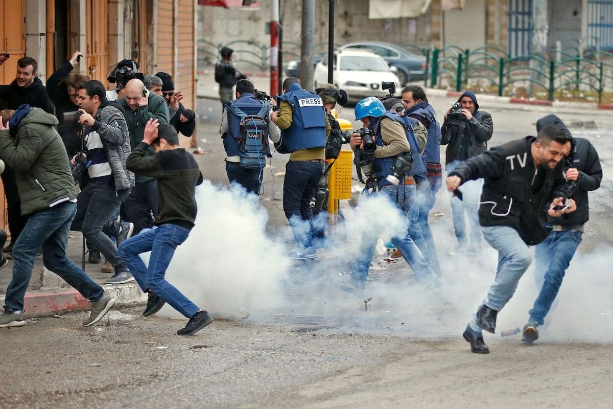 Israeli soldiers throw sound grenades at a group of people including journalists, near a gate leading to Hebron's main al-Shuhada street, closed by troops earlier in February, during an annual demonstration in memory of the 1994 Ibrahimi Mosque massacre, in the divided West Bank city of Hebron, on 22 February 2019. [HAZEM BADER/AFP via Getty Images]