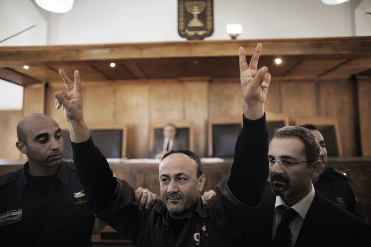 Palestinian Fatah leader Marwan Barghuti flashes the V-sign of victory as he is escorted by Israeli police into Jerusalem's Magistrate Court to testify as part of a US civil lawsuit against the Palestinian leadership, on 25 January 2012. [MARCO LONGARI/AFP via Getty Images]
