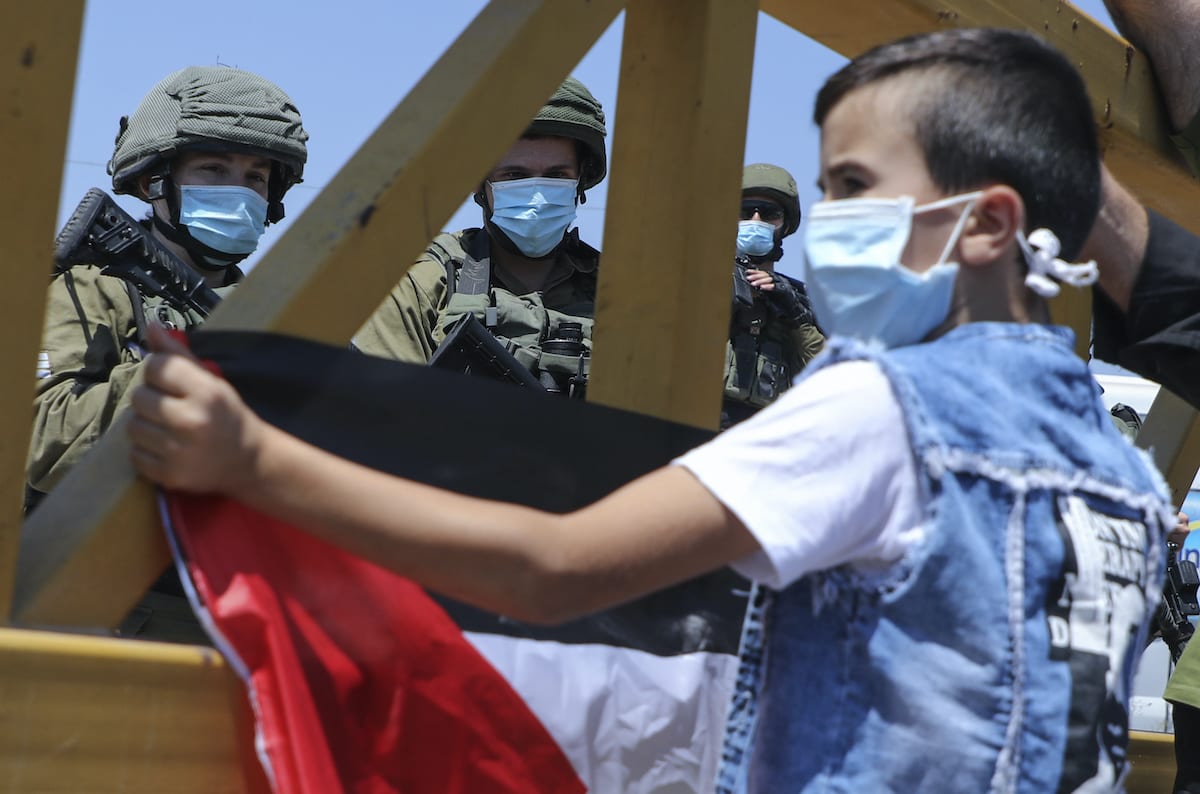 Israeli security forces look at a Palestinian boy lifting a national flag during a rally to protest Israel's plan to annex parts of the occupied West Bank, in the village of Haris, southwest of Nablus, on 28 August 2020. [JAAFAR ASHTIYEH/AFP via Getty Images]