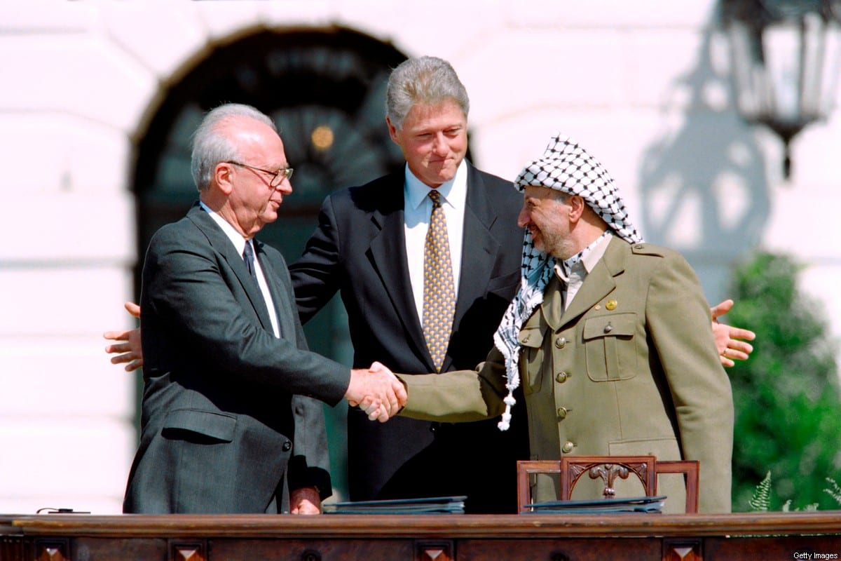 US President Bill Clinton (C) stands between PLO leader Yasser Arafat (R) and Israeli Prime Minister Yitzahk Rabin (L) as they shake hands for the first time, at the White House in Washington DC on September 13, 1993 [Photo by J. DAVID AKE/AFP via Getty Images]