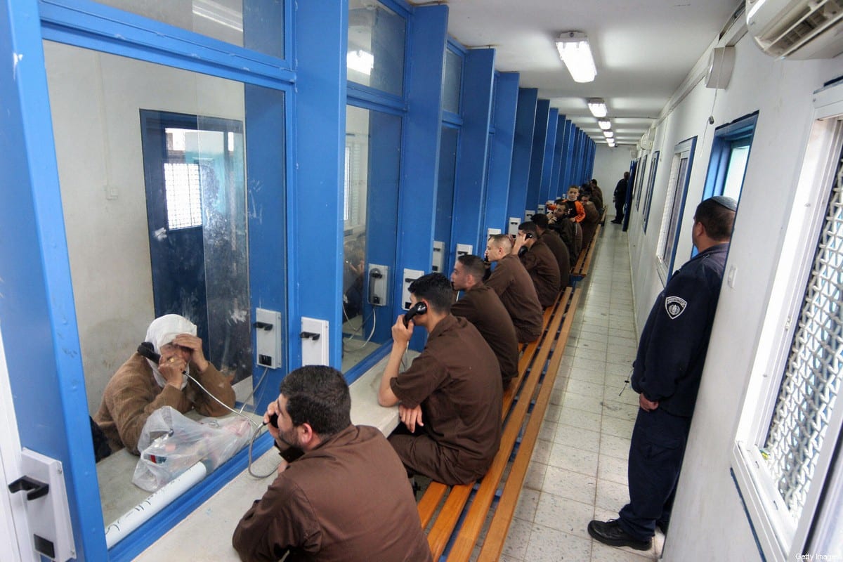 Palestinian men sit in their brown prison uniforms behind glass talking on phones to relatives 05 March 2006 at the Gilboa prison, Israel [HAGAI AHARON/AFP via Getty Images]