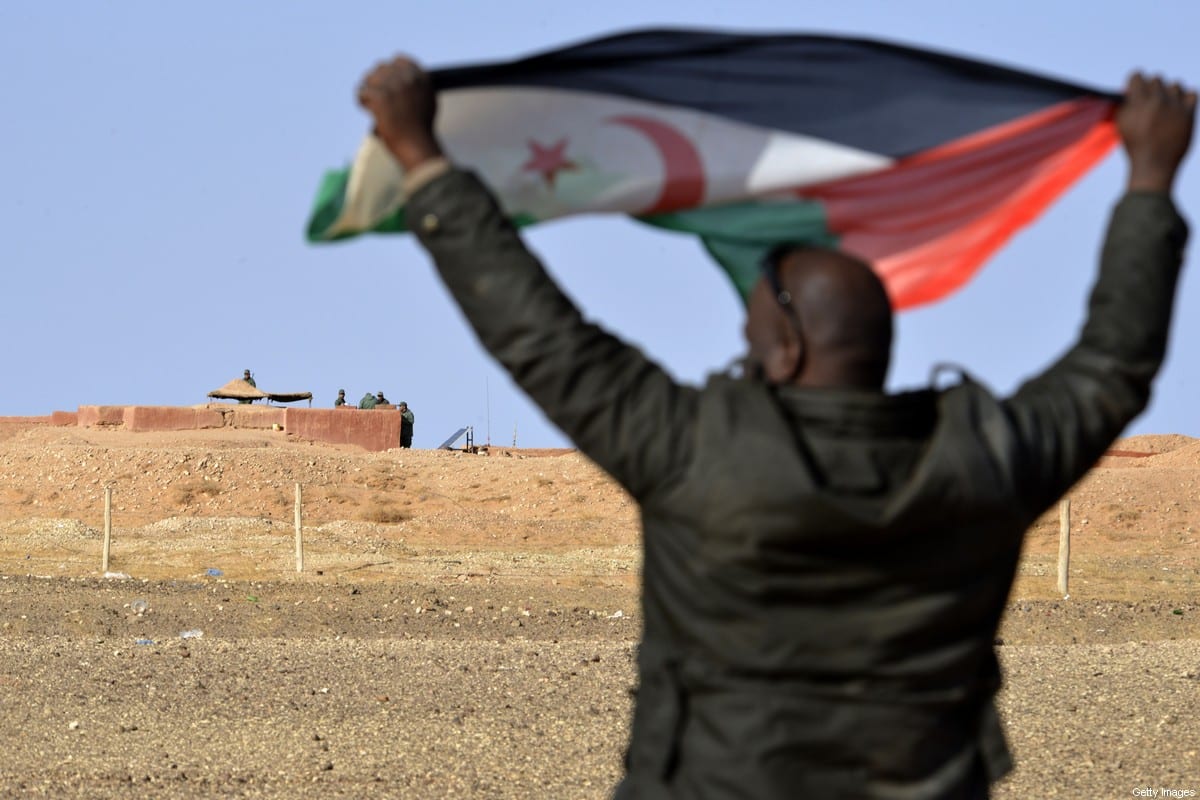 A Saharawi man holds up a Polisario Front flag in the Al-Mahbes area near Moroccan soldiers guarding the wall separating the Polisario controlled Western Sahara from Morocco on 3 February 2017. [STRINGER/AFP via Getty Images]