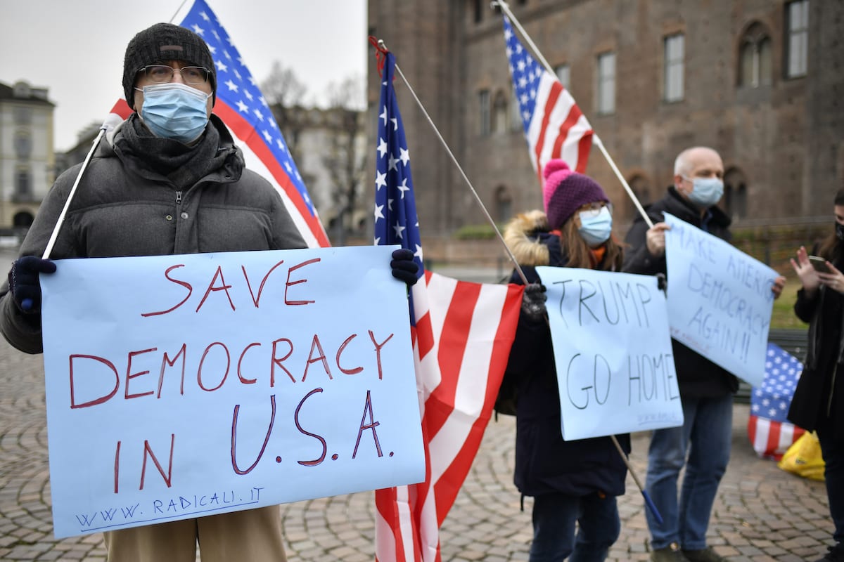 People wearing protective mask waving the American flags and holding a protest signs that reads "Trump Go Home" and "Save democracy in USA" at Piazza Castello on January 09, 2021 in Turin, Italy [Stefano Guidi/Getty Images]