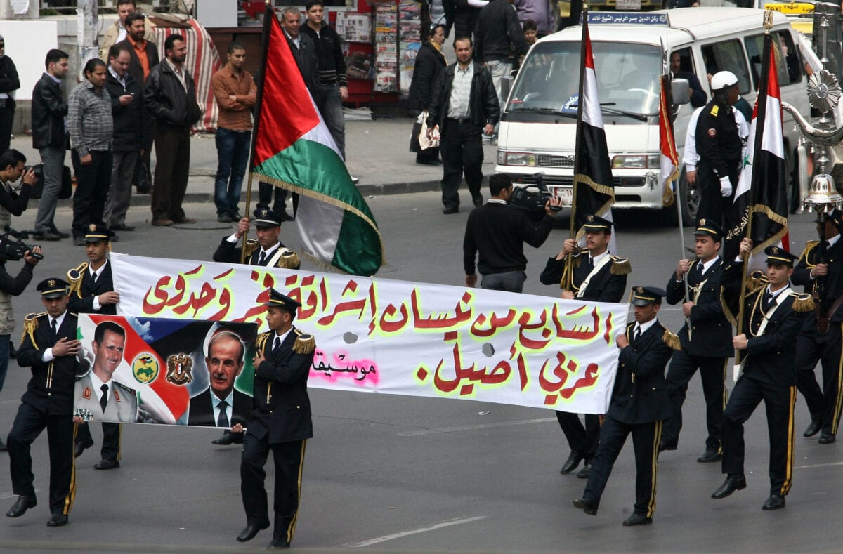 Members of a Syrian military band hold a poster showing Syrian President Bashar al-Assad (L) and his late father and predecessor Hafez al-Assad during a parade marking the anniversary of the Baath party in Damascus on April 7, 2011 [AFP via Getty Images]