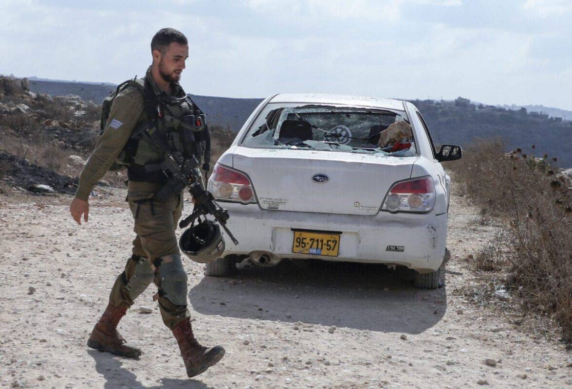 An Israeli soldier walks past a damaged car in the Palestinian village of Qusra in the occupied West Bankfollowing a reported attack by settlers on September 26, 2020 [JAAFAR ASHTIYEH/AFP via Getty Images]