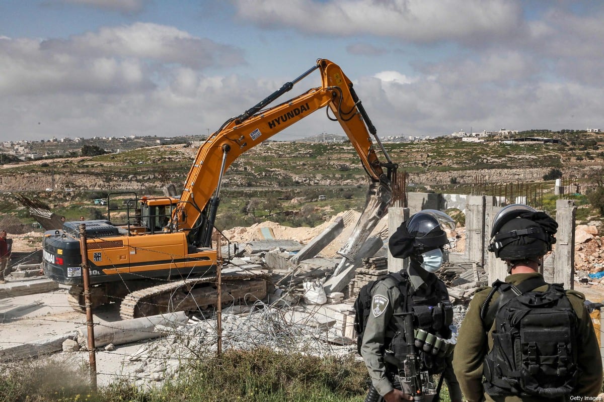 An Israeli soldier and border guard stand by as an excavator demolishes a Palestinian house (still under construction) located within the area C in the occupied West Bank on March 8, 2021 [HAZEM BADER/AFP via Getty Images]