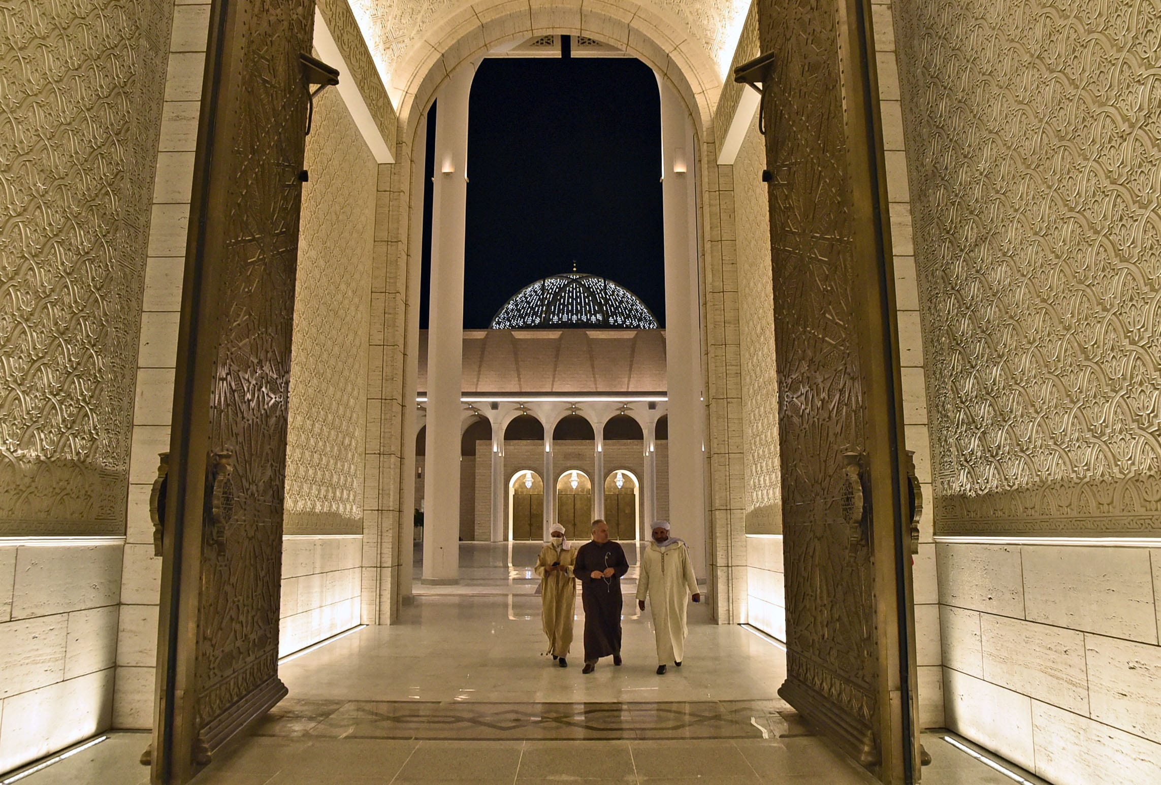 A picture taken on October 28, 2020 shows imams walking through the front door of the Great Mosque of Algiers, also known as Djamaa el-Djazair, during its inauguration in the Algerian capital. - Algeria's Grand Mosque, the world's third-biggest and Africa's largest, hosted its first public prayers yesterday, a year and a half after construction was completed. Known locally as the Djamaa El-Djazair, the modernist structure extends across 27.75 hectares (almost 70 acres), and is smaller only than the two mosques in Mecca and Medina, Islam's holiest sites, in Saudi Arabia. (Photo by RYAD KRAMDI / AFP) (Photo by RYAD KRAMDI/AFP via Getty Images)