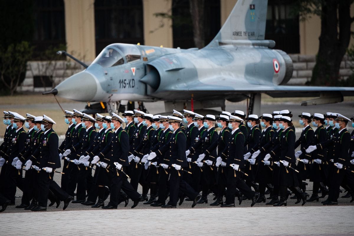 The 2019 promotion of Air School officer cadets wearing protective masks walk past a French air force Dassault Mirage 2000C fighter jet during their baptism ceremony on the Salon-de-Provence air base yard on 24 July 2020. [CLEMENT MAHOUDEAU/AFP via Getty Images]