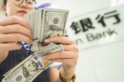 A Chinese bank employee counts US dollar bills at a bank counter in Nantong in China's eastern Jiangsu province on August 6, 2019. [STR/AFP via Getty Images]
