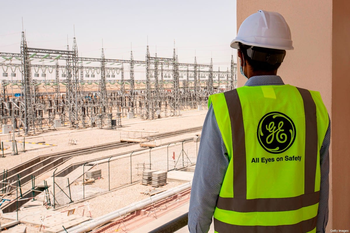 A mask-clad General Electric employee tours the Dhi Qar Combined Cycle Power Plant near the Iraqi city of Nasiriyah. [Photo by HUSSEIN FALEH/AFP via Getty Images]