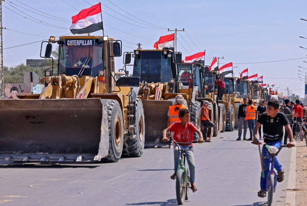 Palestinian boys cycle past a convoy of bulldozers provided by Egypt arriving at the Palestinian side of the Rafah border crossing between Egypt and the Palestinian Gaza Strip enclave on June 4, 2021 [SAID KHATIB/AFP via Getty Images]