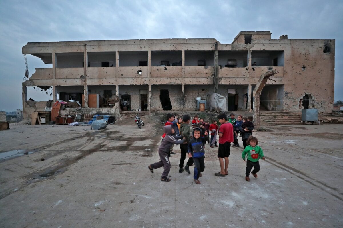 Children of displaced families living in an abandoned damaged school building, play in the yard in Binnish in Syria's northwestern province of Idlib, on March 2, 2021 [OMAR HAJ KADOUR/AFP via Getty Images]