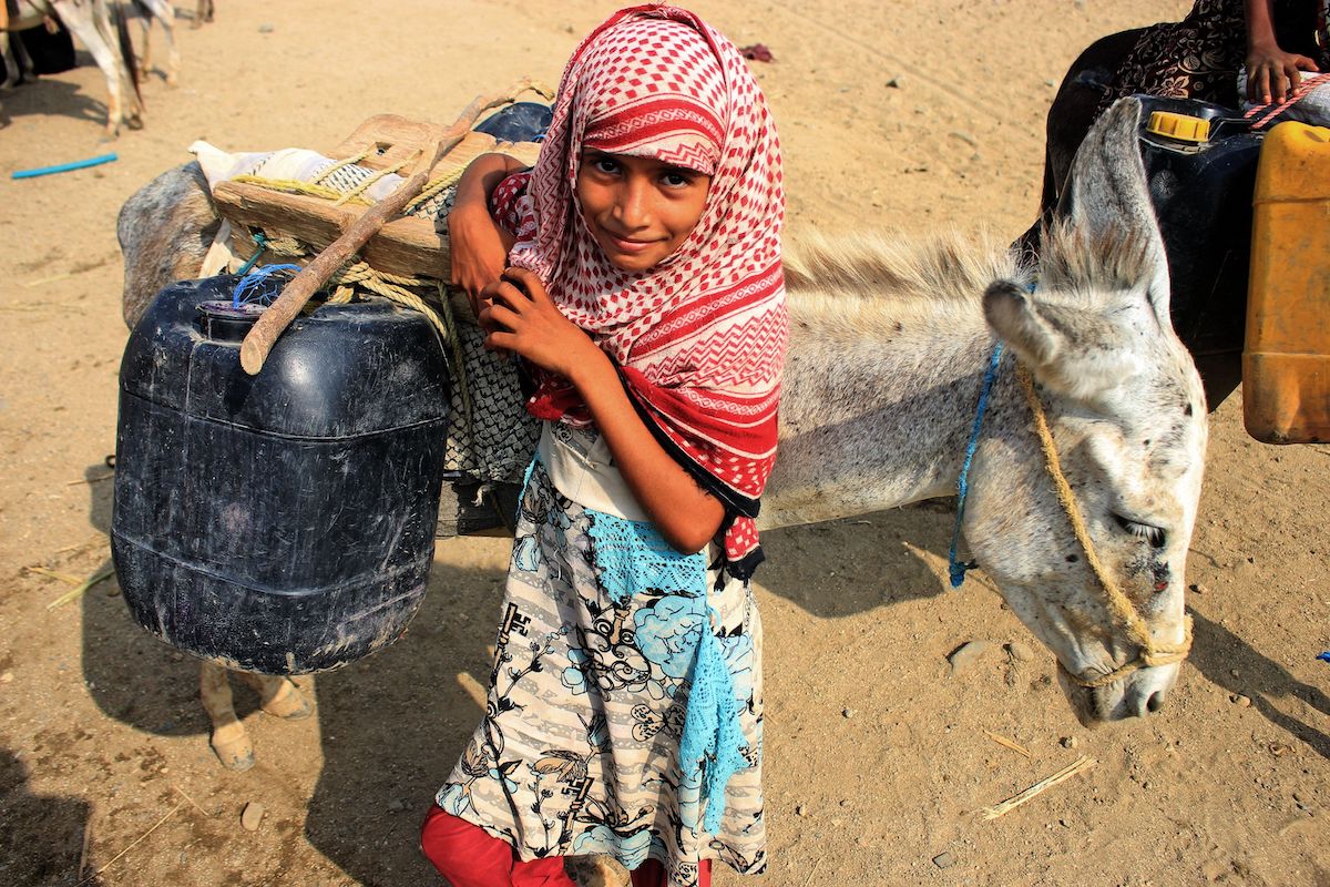 A girl stands by a donkey carrying jerrycans of water filled from a cistern at a make-shift camp for the internally displaced in Yemen's northern Hajjah province on 12 July 2021, amidst an extreme heat wave and severe water shortage. [ESSA AHMED/AFP via Getty Images]
