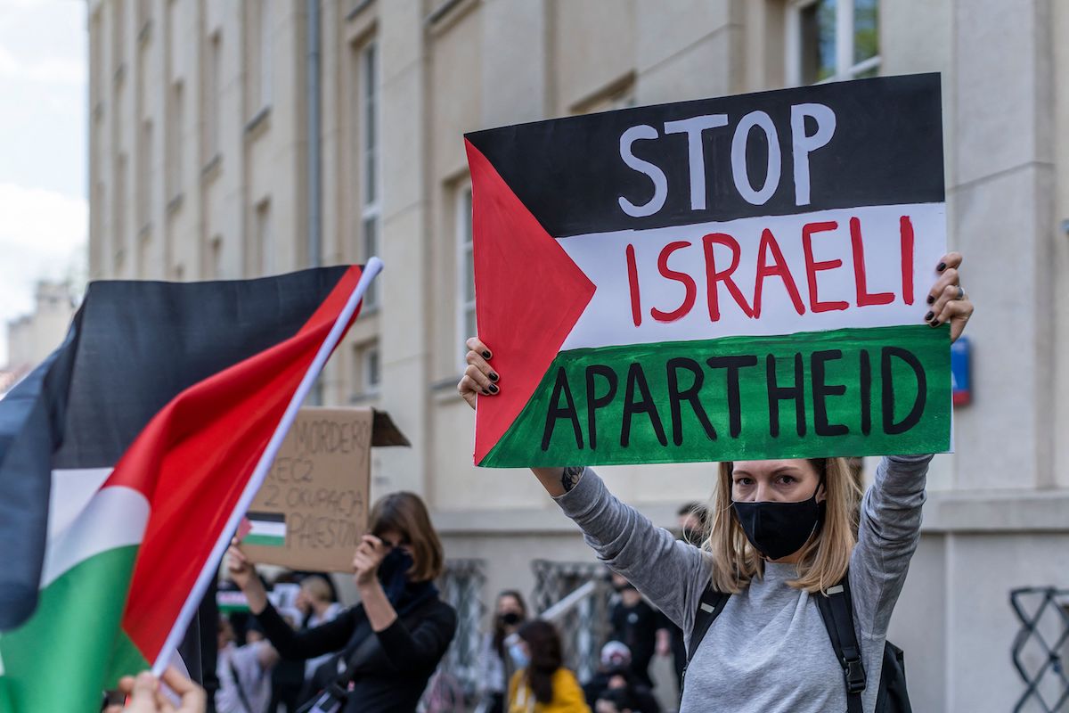 A participant holds up a sign reading "Stop Israeli Apartheid" during a protest in solidarity with the Palestinians called over the ongoing conflict with Israel in front of the Israeli embassy in Warsaw, 15 May 2021. [WOJTEK RADWANSKI/AFP via Getty Images]