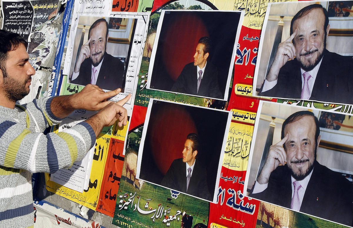 A member of the Alawite community pastes on a wall, in the northern Lebanese city of Tripoli 06 December 2007, pictures of Syrian opposition leader Rifaat al-Assad (R) and his son Ribal. Rifaat al-Assad is the younger brother of the late Syrian President Hafez al-Assad, and the uncle of the current one, Bashar al-Assad, all of whom come from the minority Alawite Muslim sect. [RAMZI HAIDAR/AFP via Getty Images]