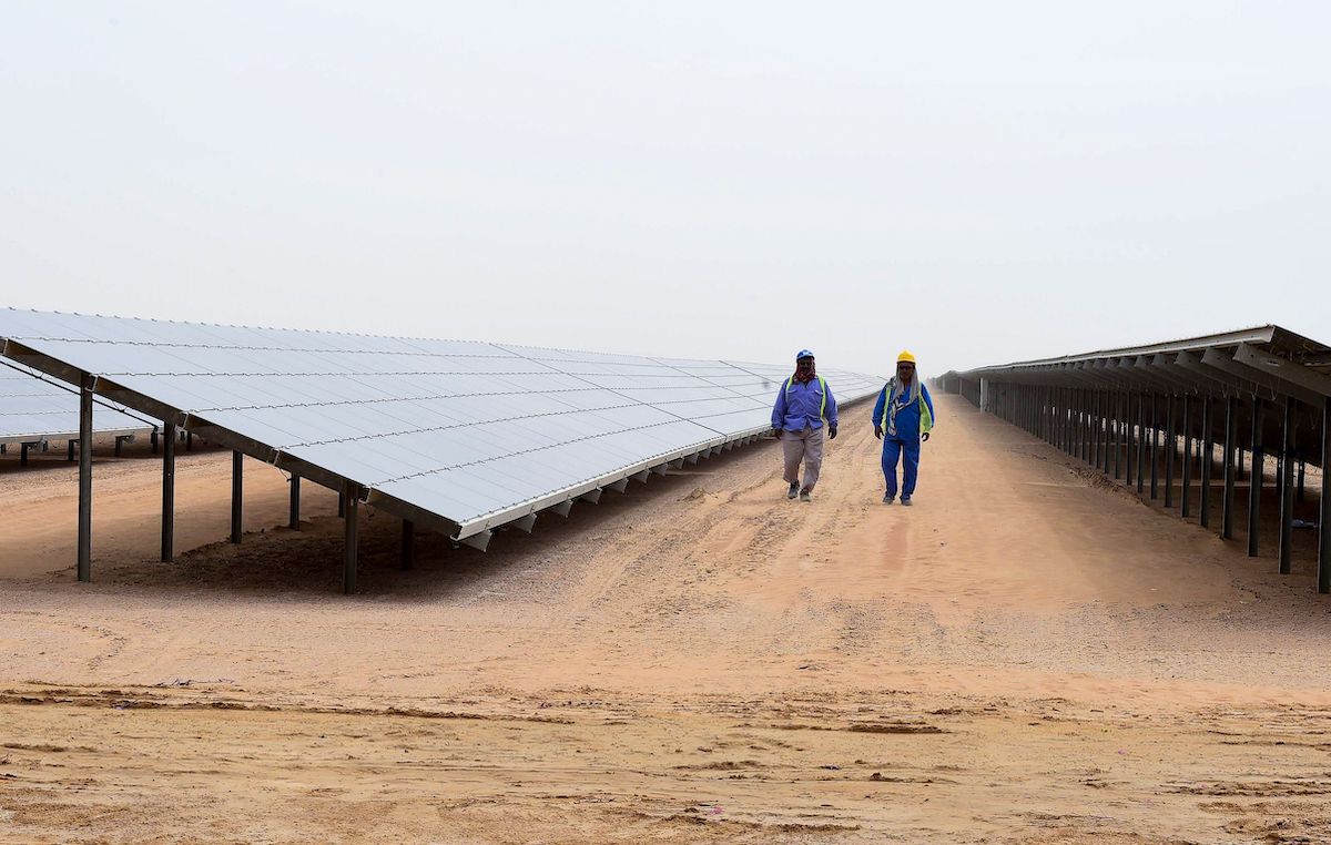 Employees walk past solar panels at the Mohammed bin Rashid Al-Maktoum Solar Park on 20 March 2017, in Dubai. [STRINGER/AFP via Getty Images]