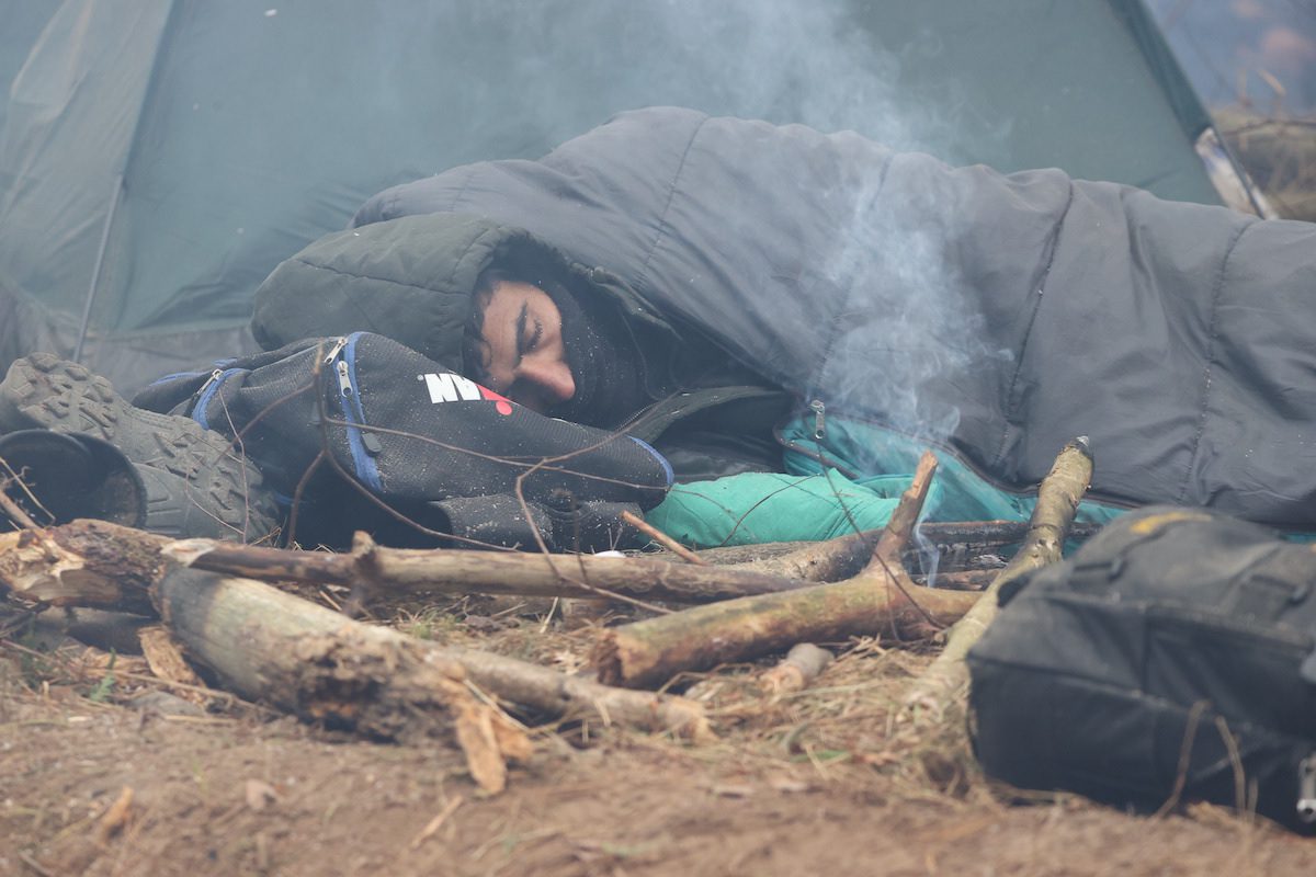 A migrant sleeps outside his tent at the Polish-Belarusian border on 10 November 2021 [Stringer/Anadolu Agency]