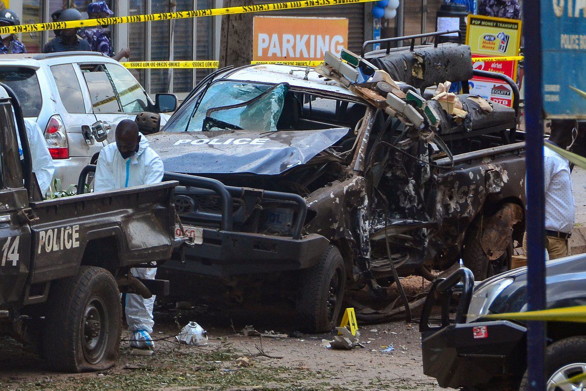 Police officers in Personal Protective Equipment (PPE) investigate around the police cars destroyed by a bomb explosion in front of Central Police Station in Kampala, Uganda, on 16 November 2021 [LAWRENCE KITATTA/AFP/Getty Images]