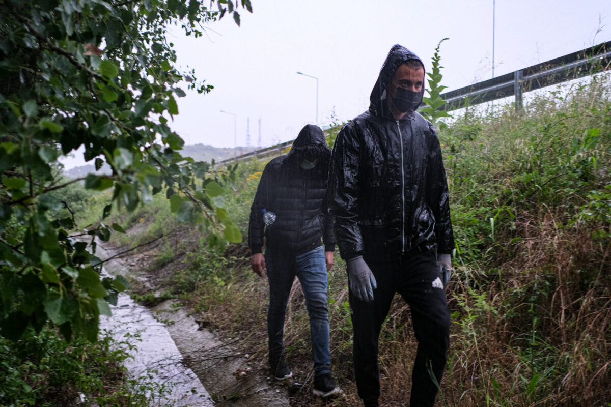 An Algerian and a Palestinian asylum seeker walk through the woods in a downpour near the side of a highway as they crossed into Greece from from Turkey on June 13, 2021 in Lyra, Greece [Byron Smith/Getty Images]