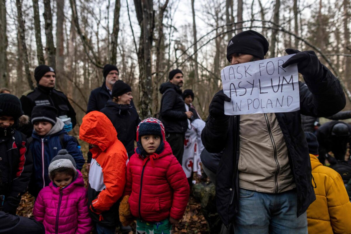 A member of a Kurdish family from Dohuk in Iraq holds a paper reading 'I ask for asylum in Poland' as they wait for the border guard patrol, near Narewka, Poland, near the Polish-Belarus border on November 9, 2021 [WOJTEK RADWANSKI/AFP via Getty Images]
