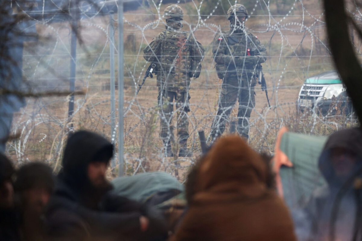 A picture taken on November 10, 2021 shows Poland's servicemen behind a barbed wire fence on the Belarusian-Polish border as they watch migrants camping on the Belarusian side in the Grodno region [RAMIL NASIBULIN/BELTA/AFP via Getty Images]