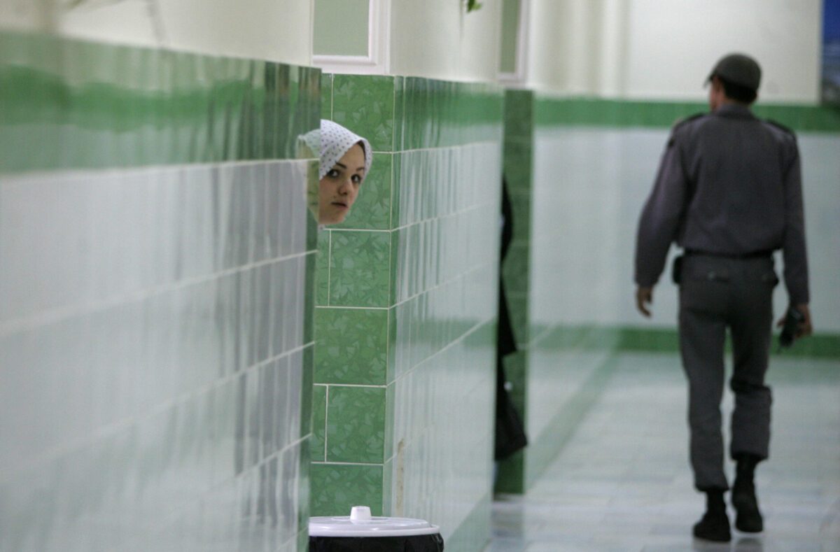 Tehran, IRAN: TO GO WITH AFP STORY IRAN-JUSTICE-PRISON-SOCIT BY PIERRE CELERIER An Iranian inmate peers from behind a wall as a guard walks by at the female section of the infamous Evin jail, north of Tehran, 13 June 2006. AFP PHOTO/ATTA KENARE (Photo credit should read ATTA KENARE/AFP via Getty Images)