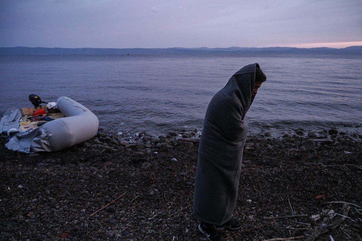 A migrant covered with a blanket stands on a beach near Skala Sykamineas after crossing the Aegean sea between Turkey and Greece on 1 March 2020 [ARIS MESSINIS/AFP/Getty Images]