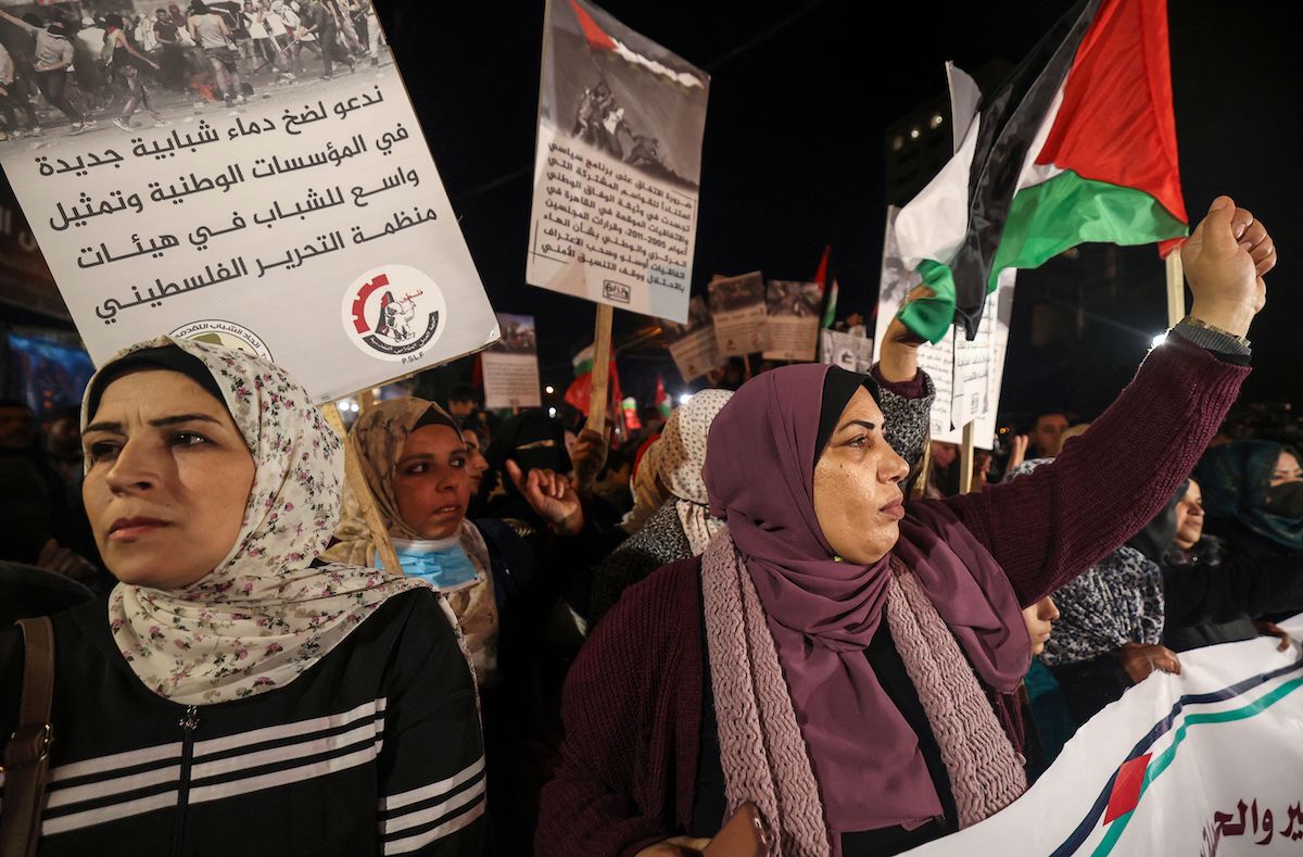 Palestinian supporters of the Popular Front for the Liberation of Palestine (PLFP) lift placards and national flags during a rally in Gaza city on 6 February 2022, to protest the meeting of the Palestine Liberation Organization's (PLO) Central Committee in Ramallah. [MAHMUD HAMS/AFP via Getty Images]