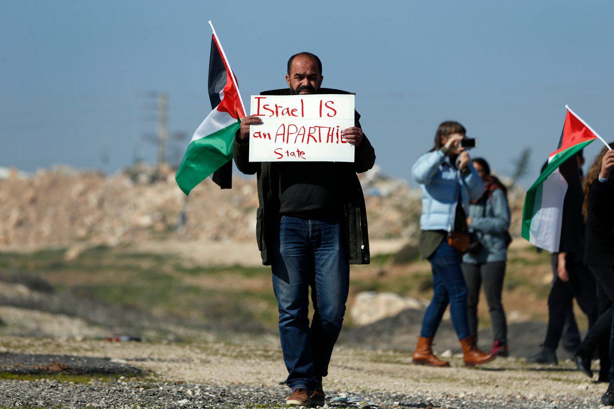 A protestor carries a sign reading 'Israel is an apartheid state' during a demonstration in the West Bank, 23 January 2019 [ABBAS MOMANI/AFP/Getty Images]