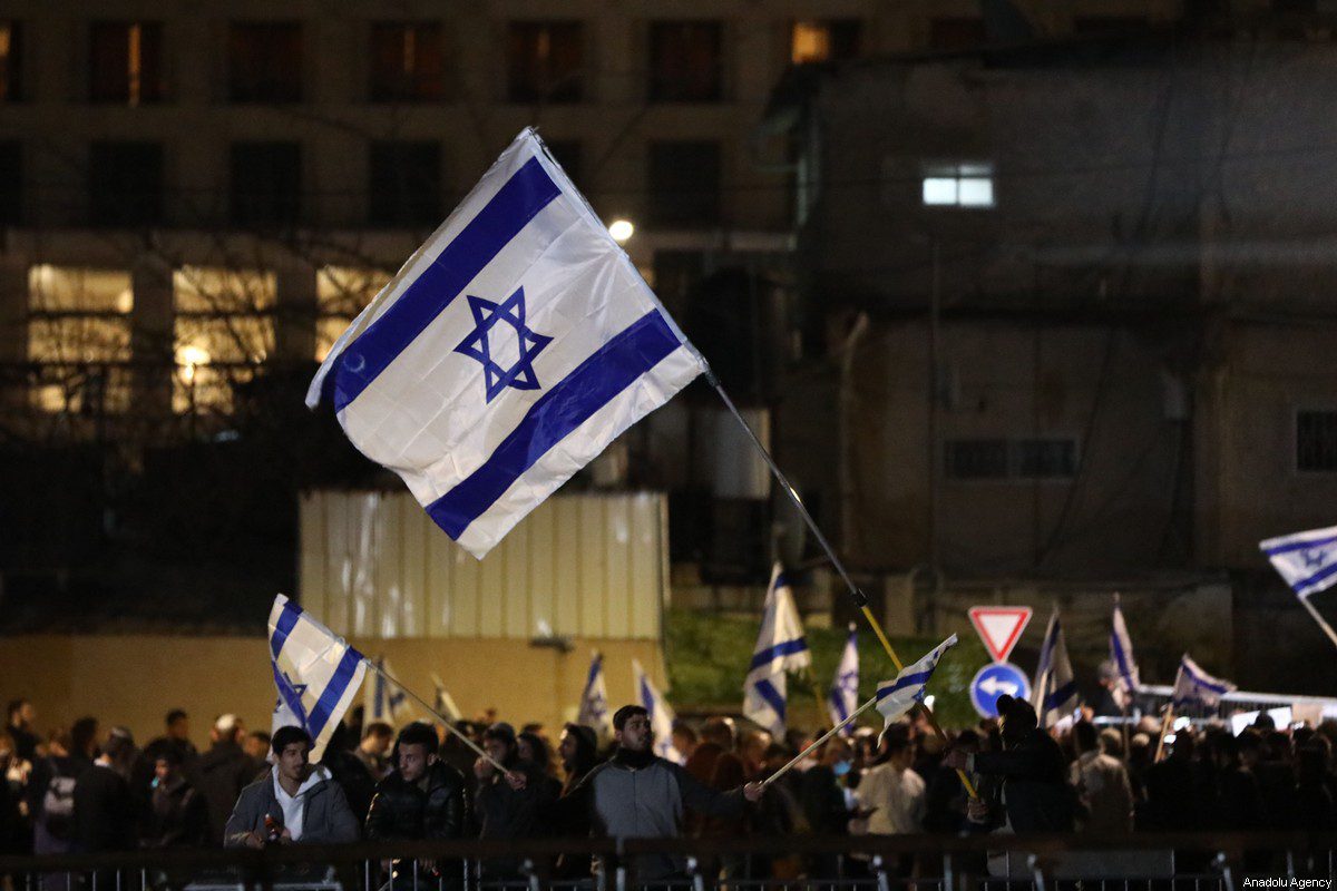 Jewish settlers wave Israeli flags during a gathering in a parking lot near Palestinian Salem's house, who were facing imminent expulsion, after the court ruled four Palestinian families to remain in their houses in Sheikh Jarrah neighborhood in East Jerusalem on 2 March 2022. [Mostafa Alkharouf - Anadolu Agency]