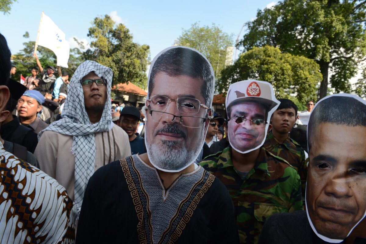 Demonstrators wear a masks bearing the portrait of ousted Egyptian president Mohamed Morsi (C), next to his "enemies" including US former President Barack Obama (R) on August 16, 2013 [ROMEO GACAD/AFP via Getty Images]