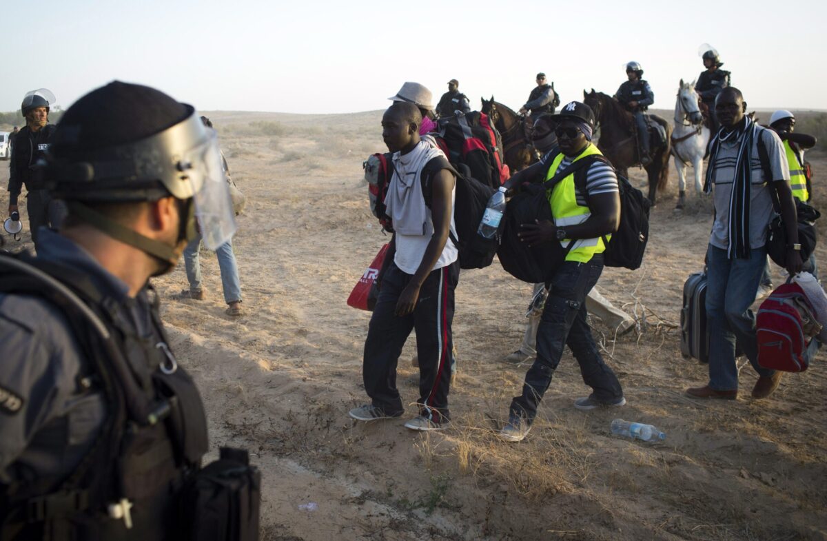 Israeli policemen and immigration officers watch as African asylum seeker move on after spending the last two days protesting in an outdoor camp near the Nitzana border crossing with Egypt in the Negev Desert on June 29, 2014. Nearly 1,000 illegal African immigrants in Israel staged a march from Holot detention center towards the southern border with Egypt to protest against living conditions in the Holot detention center. The Israeli population and immigration office said that in late 2013 there were 53,646 African immigrants in Israel, 35,987 of whom were Eritrean, 13,249 Sudanese and the remainder from other countries. AFP PHOTO/OREN ZIV ==ISRAEL OUT== (Photo credit should read OREN ZIV/AFP via Getty Images)