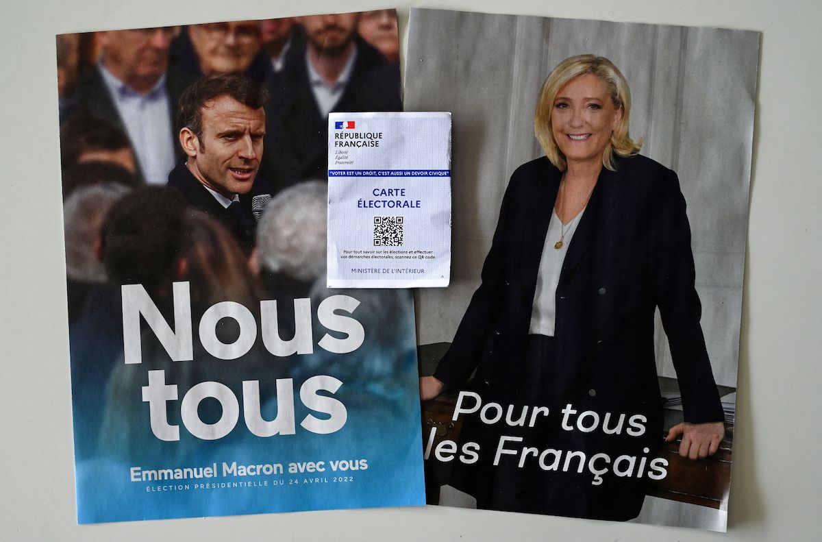 An electoral card is shown in front of posters of far-right Party (RN) presidential candidate Marine Le Pen (R), and incumbent President and candidate for his reelection Emmanuel Macron (L) in Montpellier, southern France, on 21 April 2022. [PASCAL GUYOT/AFP via Getty Images]