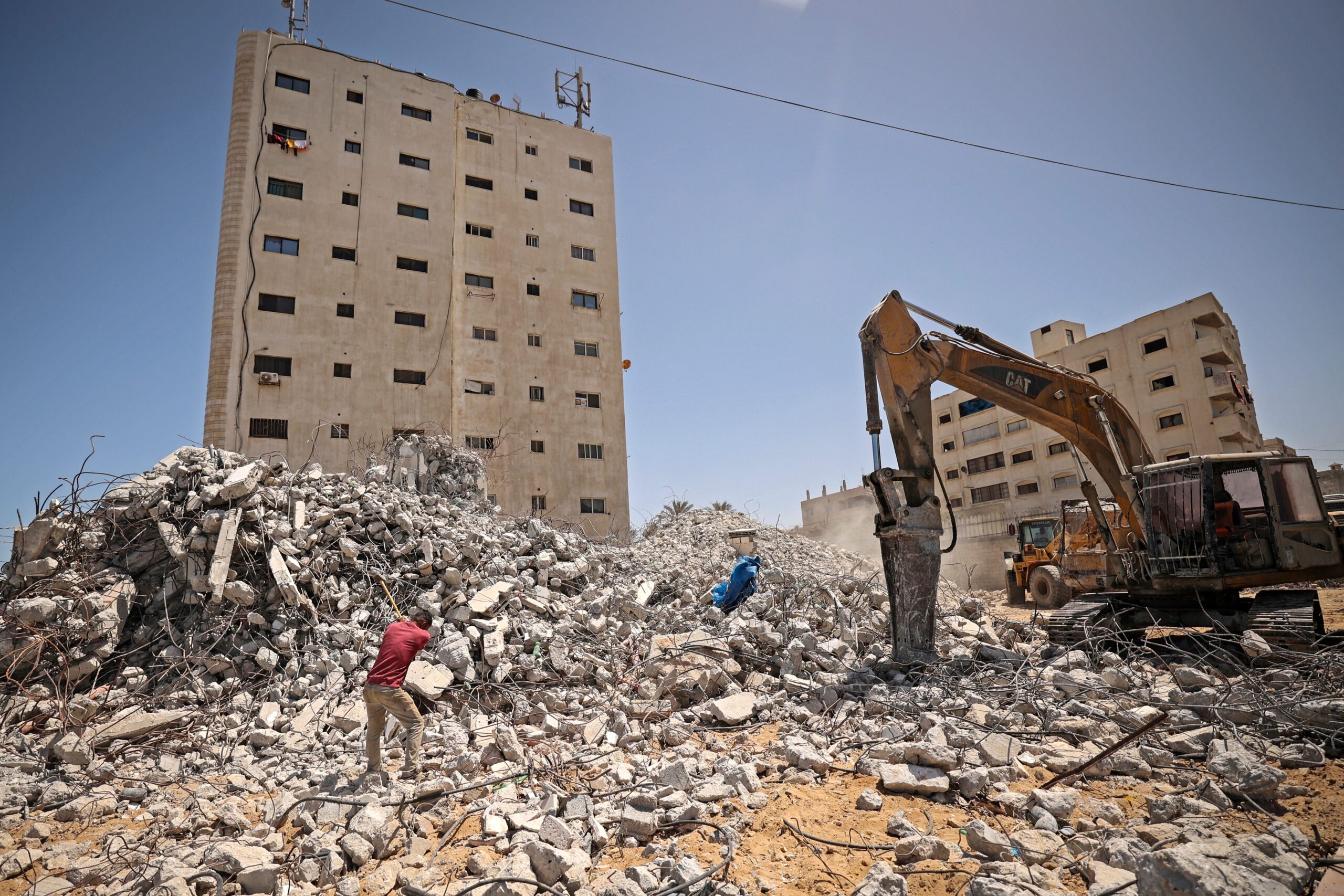 A Palestinian worker clears the rubble of a destroyed building on the first anniversary of the May 2021 conflict between Israel and Hamas, in Gaza City on May 10, 2022 [Photo by MAHMUD HAMS/AFP via Getty Images]