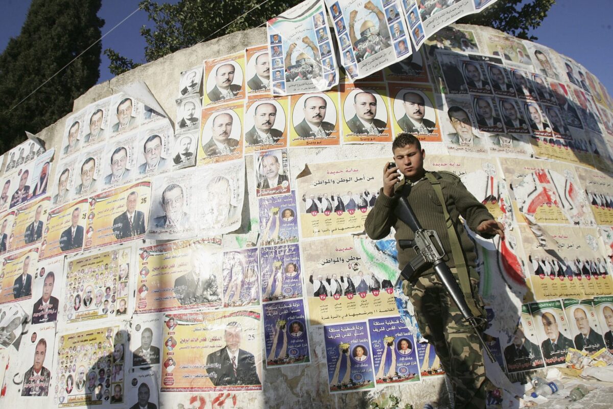 GAZA CITY, GAZA STRIP - JANUARY 22: A member of the Palestinian security forces stand next to posters of the Palestinian legislative candidates on a wall of an election station on the second voting day, January 22, 2006 in Gaza City, Gaza Strip. The newly elected Palestinian Legislative Council (PLC) will be expanded, and half of the seats will be allotted by proportional representation of all parties that gather more than two percent of the vote. (Photo by Abid Katib/Getty Images)