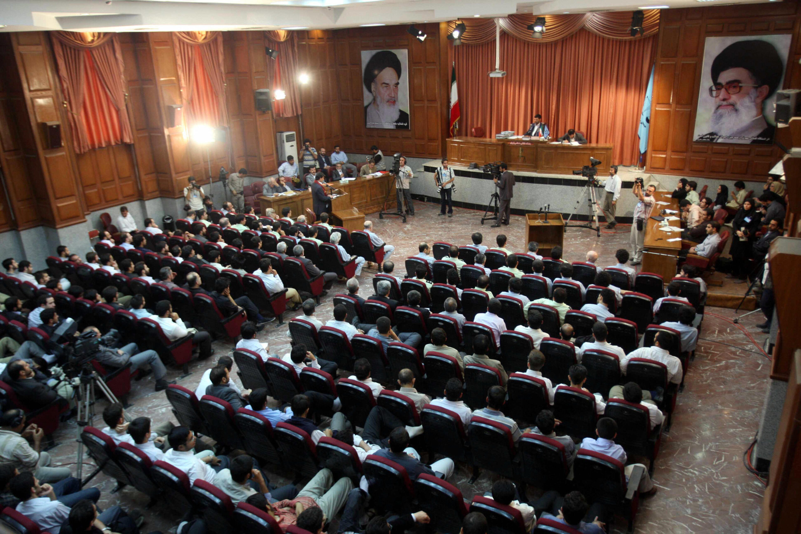 A general view of a courtroom shows suspected opposition supporters (in grey) attending the latest session in their trial at the revolutionary court in Tehran on August 25, 2009. Several aides to former Iranian president Mohammad Khatami and top reformists were put on trial on charges of masterminding the post-election unrest which rocked the Islamic republic. Among the some 20 people in the dock were a former minister and a number of other top political figures as well as journalists and academics. Portraits on the wall show the Islamic republic's supreme leader Ayatollah Ali Khamenei (R) and his predecessor, the late Ayatollah Ruhollah Khomeini. AFP PHOTO/FARS NEWS/HASSAN GHAEDI (Photo credit should read Hassan Ghaedi/AFP via Getty Images)