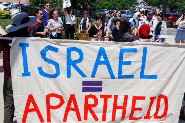 Protesters stand are holding a banner that equates Israel with apartheid [Stephen Zenner/SOPA Images/LightRocket via Getty Images]